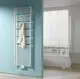 Kermi-Heizkörper, vertikal montiert, mit horizontalen Rippen in einem Badezimmer, neben einer Badewanne und einer hellen Wand. Ein Handtuch hängt daran.